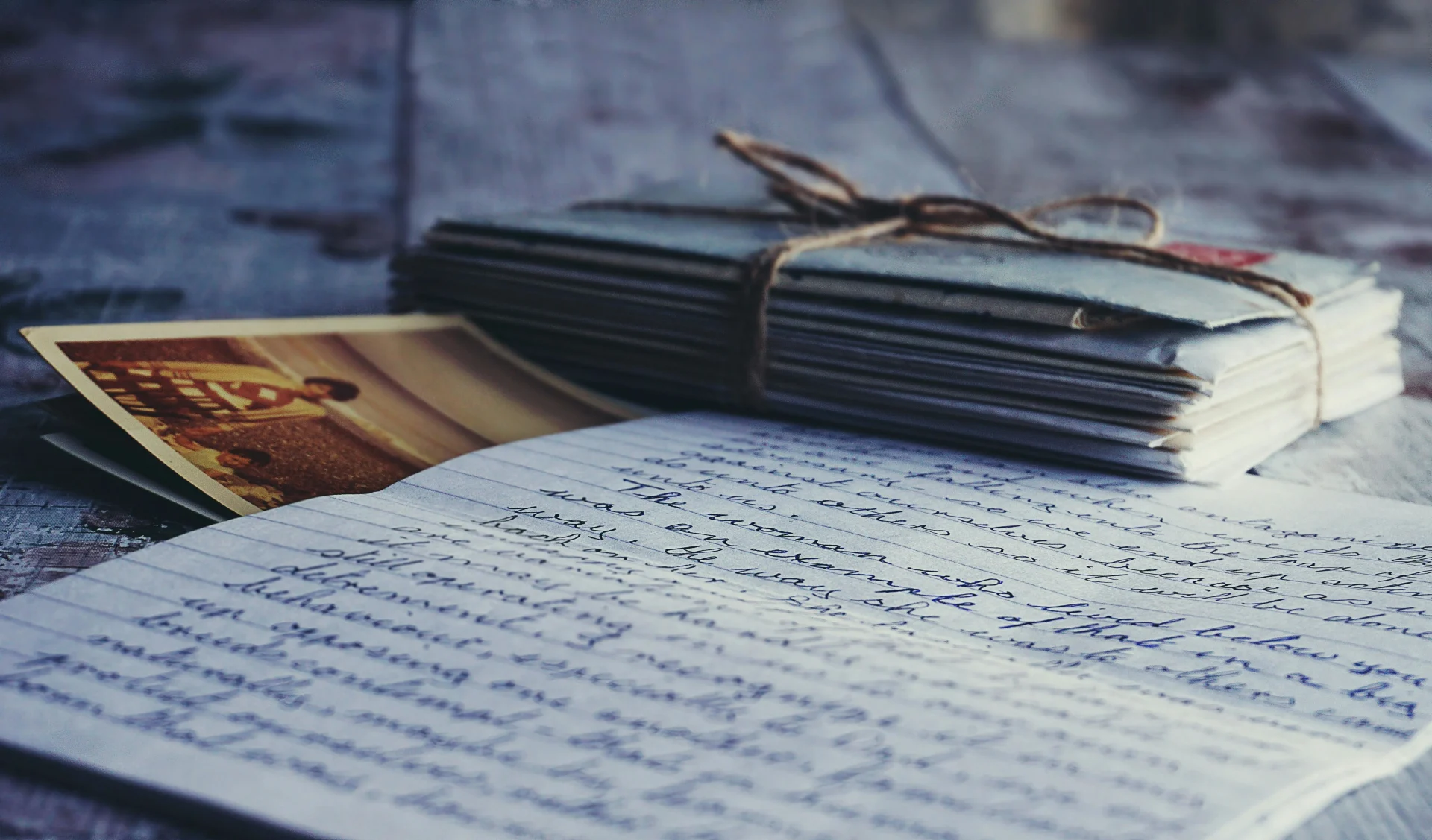 A wooden table displays a notebook alongside a photo and a letter, evoking a sense of nostalgia and personal reflection
